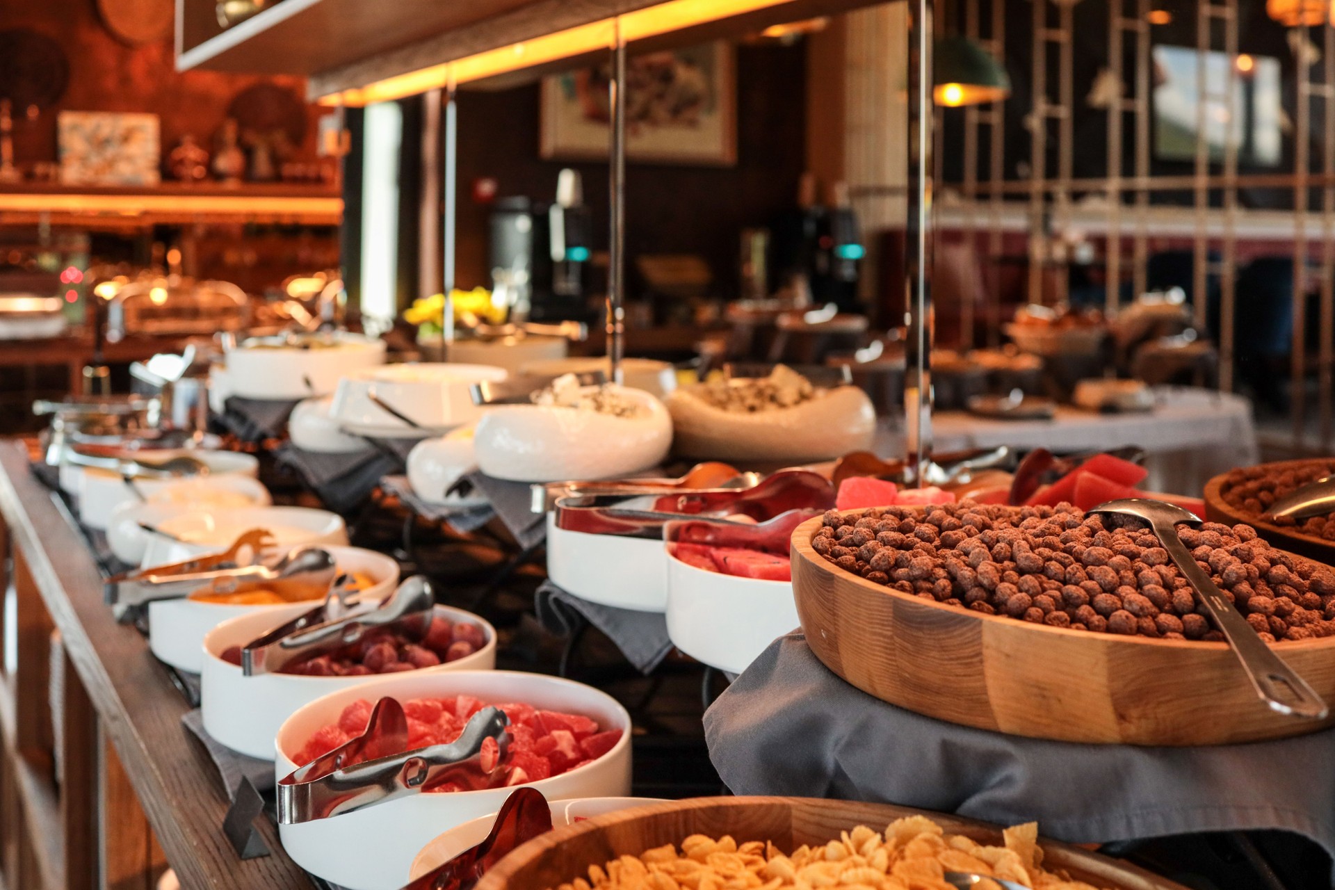 Rich hotel breakfast buffet with bowls of fresh fruits, cereals, nuts, cheeses, and cold cuts. Close-up view of a variety of colorful dishes on a stylish counter with serving utensils